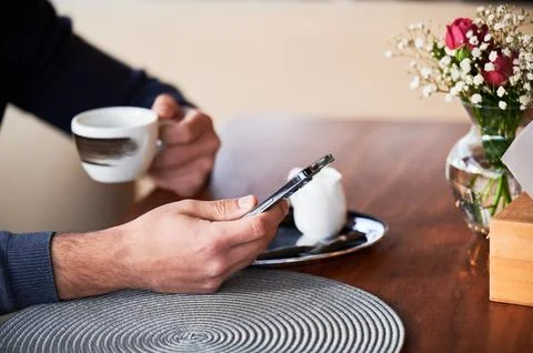 Close up of man using smartphone while holding coffee cup at cafe table Stock Photos
