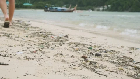 Close-up of man walking along polluted beach with plastic waste and debris on Stock Footage 287350267