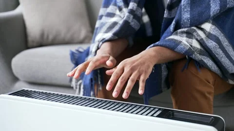 Close up of man warming hands by holding near heater and rubbing them together  Video stock 297876851