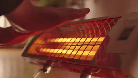 Close-Up of Man Warming Hands Over Infrared Heater. Cozy Indoor Heating Solution Stockbeeldmateriaal 289589046