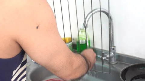 Close-up of a man washing a grill grate with his hands in the sink with water in 库存影片 155805885