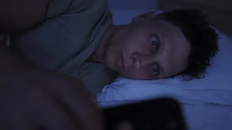 Close up of man watching content on smartphone in bed at night, excessive screen 스톡 동영상 346248012