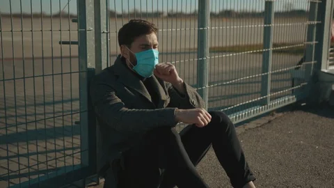 Close up man wearing Protective Face Mask sitting near fence border sneeze Stock Footage 126617234