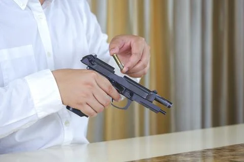 Close up man in white shirt is loading a black beretta pistol on desk in hi.. Stock Photos