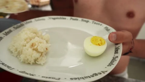 Close-up of a man without polo serving rice on a plate with a boiled egg that Vidéo 189101603