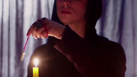 Close up of man wizard rotating a magic pendulum over a candle Stock Footage 179412334