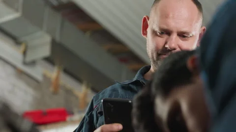 Close-Up of Man Working on Engine with Colleague Using Phone for Guidance Stock Footage 301249515