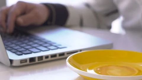 Close-up of man working on laptop and drinking tea from mug with saucer. Stock Footage 86635597