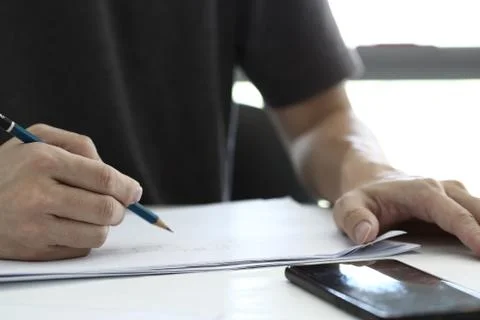 Close up man Writing on Paper on the Table in a office room. mobile device pl Stock Photos