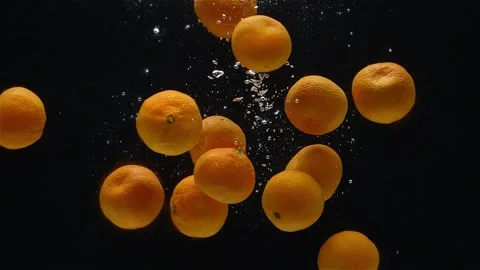 Close-up of mandarins falling down into the water against a black background. Stock Footage 272599377