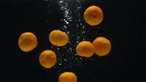 Close-up of mandarins falling down into the water against a black background. Stock Footage 272599386