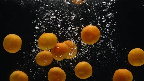 Close-up of mandarins falling down into the water against a black background. Stock-Footage 272599630