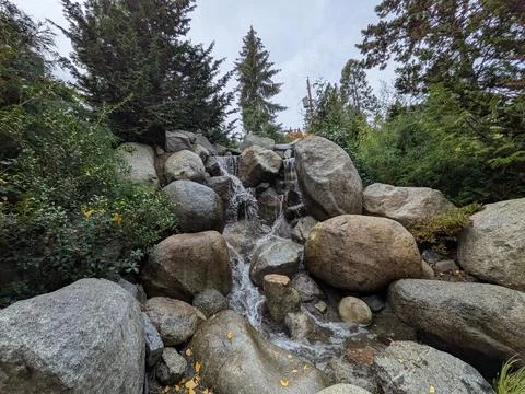 Close-up of a manmade waterfall surrounded by rocks, green trees, bushes Stock Photos