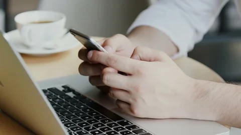 Close-up of man's arm using phone on table with laptop and coffee nearby Stock Footage 112987233