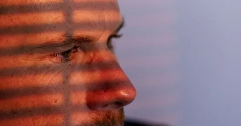 Close up on man's eyes with warm sun coming through blinds 4K Stock Footage 80229322