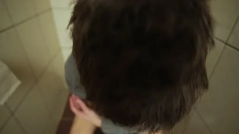 Close-up of a man's face as he sits on the toilet, tears welling in his eyes Stock Footage 303904527