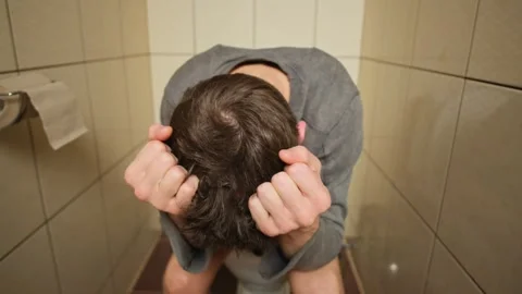 Close-up of a man's face as he sits on the toilet, tears welling in his eyes Stock Footage 307787387
