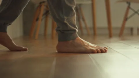 A close-up of a mans feet. Bare feet stepping on wood-patterned tiles in a h Stock Footage 323723028