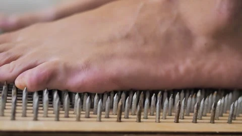 Close-up of a man's foot becoming on nails, helped by hands. Nailing. Practice. Video stock 286043645