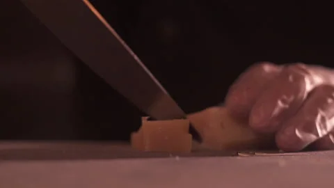 Close-up of a man's gloved hands, stabbing hard cheese into pieces with a knife. Stock Footage 155467408