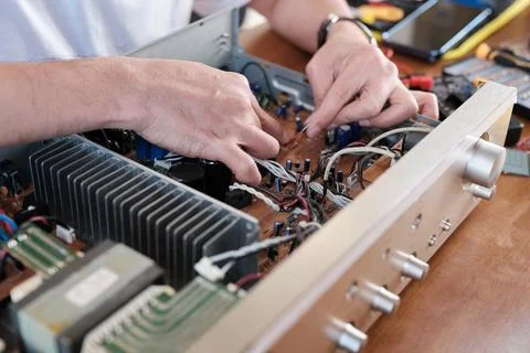 Close-up, man's hand checking audio equipment circuit board for wiring repair. Stock Photos
