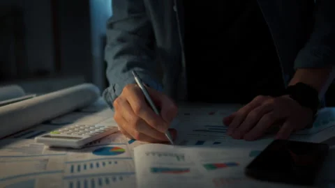 Close-up of a mans hand circling errors with a pen on paper charts spread on Stock Footage 348319541