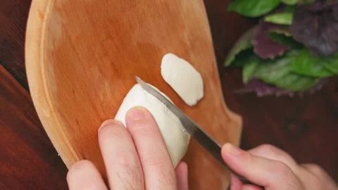 Close-up of man's hand cutting mozzarella on wooden cutting board Stock Footage 250364758