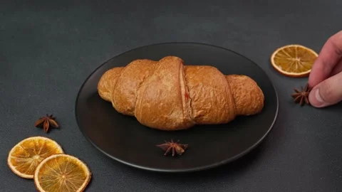 Close-up of Man's Hand Decorating Croissant Lying on black Plate Stock Footage 237313456