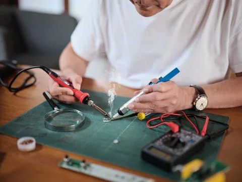 Close-up, man's hand fixing home electrical appliance, soldering circuit board. Stock Photos