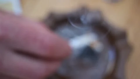 Close up of a man's hand flicking ash from a burning cigarette into a brown Stock Footage 333801023