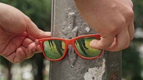 Close-up of a man's hand hanging orange sunglasses hanging from a lamppost in Stock Footage 221861669