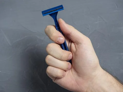 Close up of a man's hand holding a blue plastic razor on a gray textured back Stock Photos