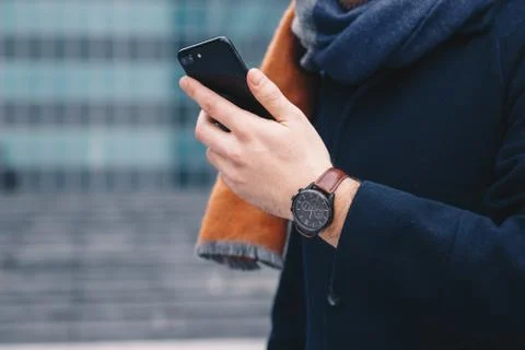 Close up of a man's hand holding a cellphone and wearing a wrist watch, in front Stock Photos