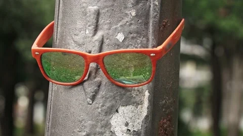 Close-up of a man's hand holding orange sunglasses hanging on a lamppost on the Stock Footage 221861660