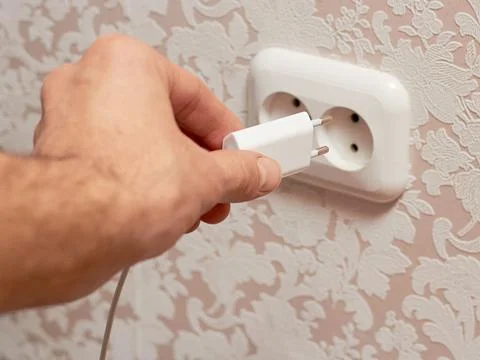 Close-up of a man's hand inserting a charger plug into a wall outlet. Stock Photos