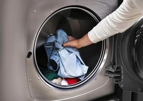 Close-up of a man's hand loading blue jeans and clothes into a modern washi.. Stock Photos