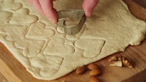 Close up man's hand making cookies, cutting hearts from dough on kitchen table. Video stock 169461060
