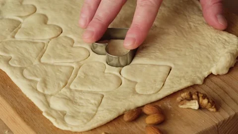 Close up man's hand making cookies, cutting hearts from dough on kitchen table. Video stock 169461497