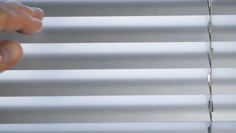 Close up man's hand moves towards closed Venetian blinds, opens slats 库存影片 128640394