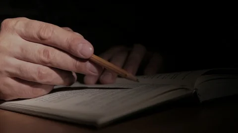 Close-up of a man's hand with an open paper book, writes a note with a pencil on Stock Footage 92613376