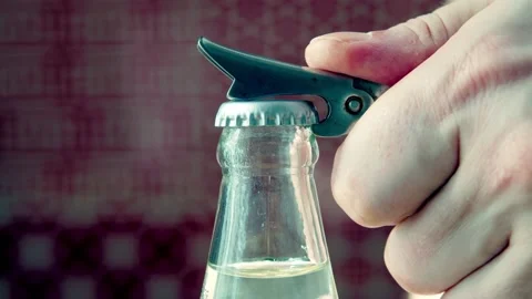 Close up a man's hand opens a bottle of mineral water with a bottle opener in an Stock Footage 166348808