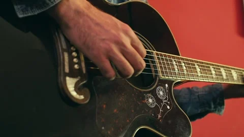 Close-up of a man's hand playing an acoustic guitar against the red background Stock Footage 248529488