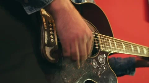 Close-up of a man's hand playing an acoustic guitar against the red background Stock Footage 248530408