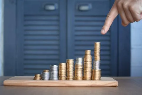 Close-up of a man's hand pointing at columns of multi-colored coins of increa Stock Photos