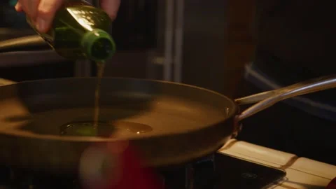 Close up of mans hand pouring olive into fry pan on stove top in home kitchen Stock Footage 234034506