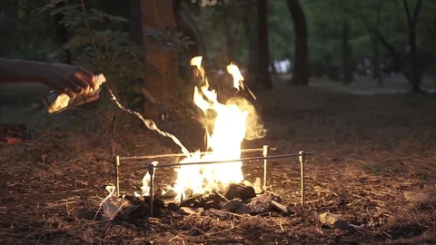 Close-up - a man's hand pours ignition on smoking embers and makes a fire.The Stock Footage 116673652