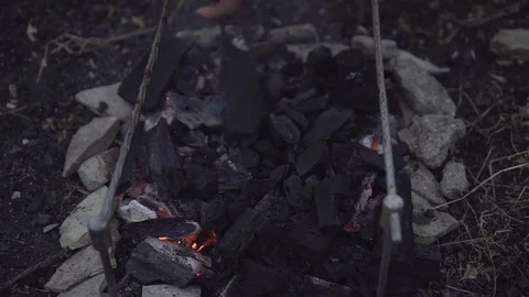 Close-up - a man's hand pours stirring smoking embers to kindle a fire. The Stock Footage 116673746