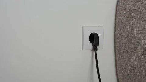 A close-up of a man's hand pulls a black power wire out of a white outlet Stock Footage 202143354