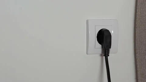 A close-up of a man's hand pulls a black power wire out of a white outlet Stock Footage 202172642