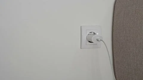 A close-up of a man's hand pulls out a white power adapter from the outlet to Stock Footage 202143275